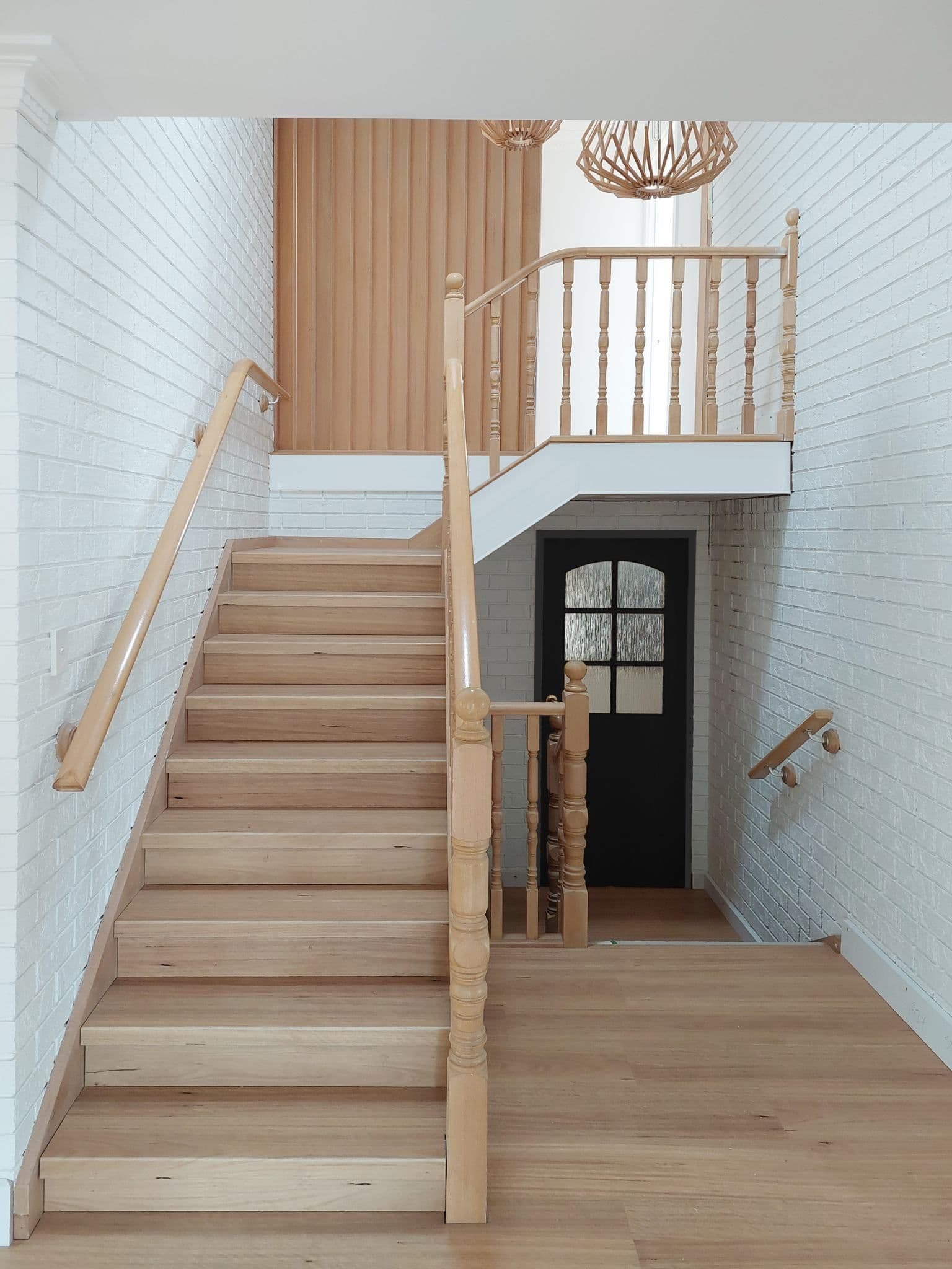 Timber staircase with white balustrade rising through a double-height void to a black entry door — a finished Tricoat interior